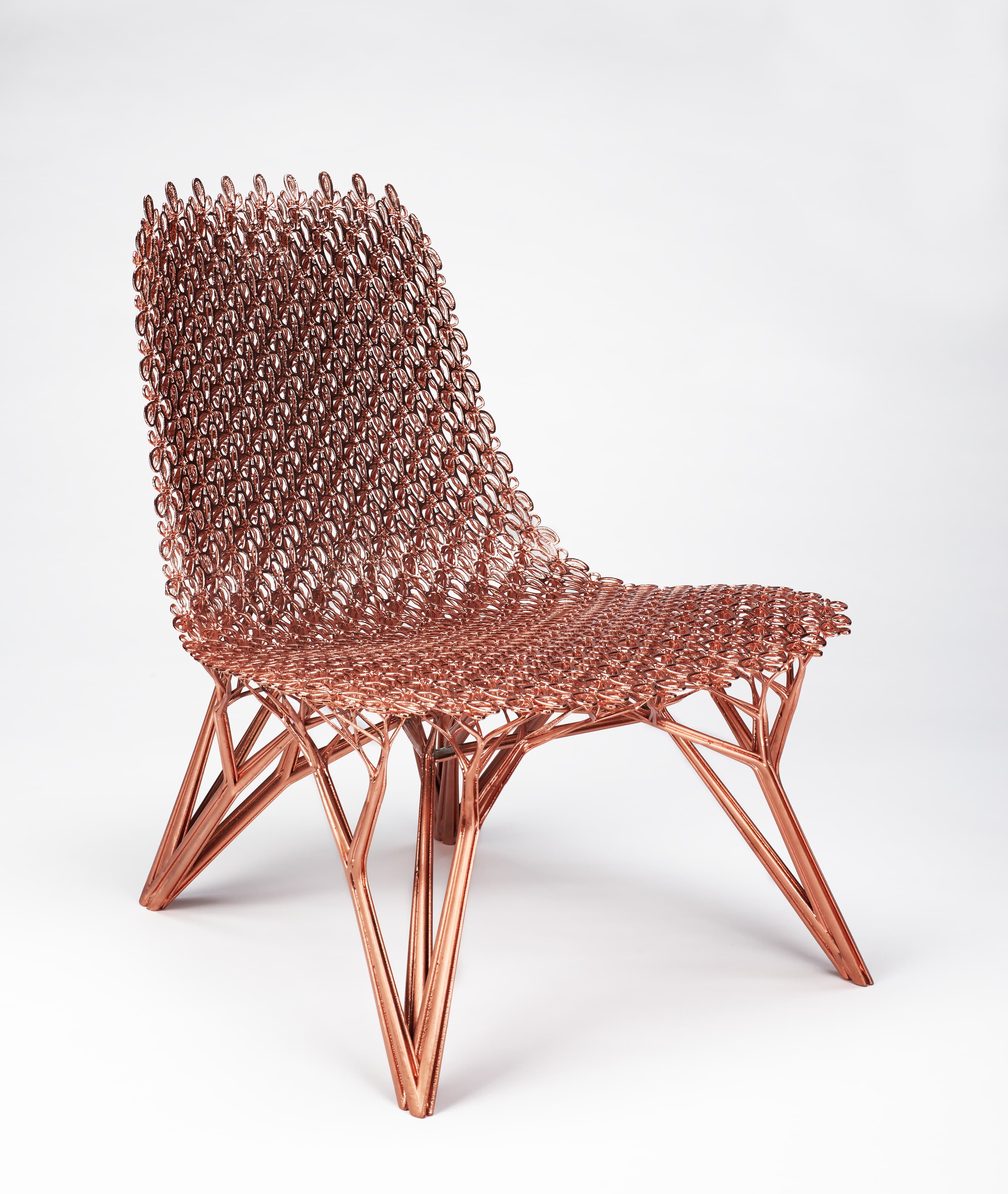 A shiny, copper-colored chair with no arms. The body of the chair is composed of a mesh of overlapping, long, vertical oval rings. From the bottom, the four legs of the chair branch upward toward the body into smaller and smaller branches, like the branches of a tree, to support the seat structure.