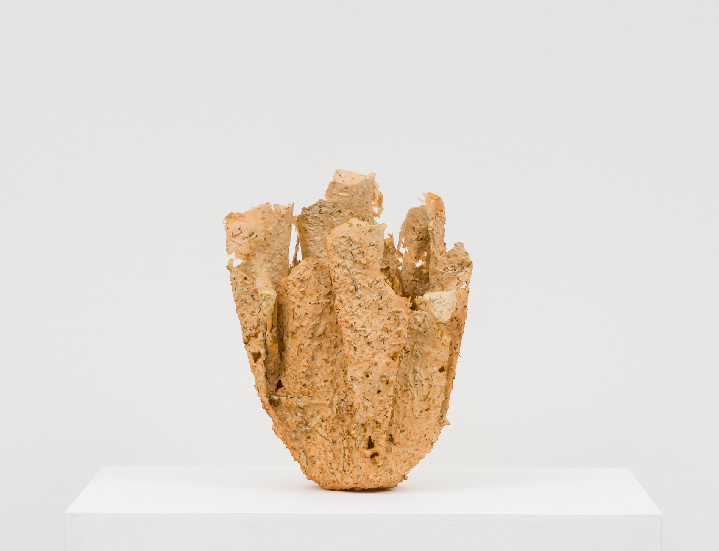 A light brown, textured basket construction. It is made of desert matter mixed with natural pulp. The basket has a flat base and gentle folds that reach upward into several points at the top.