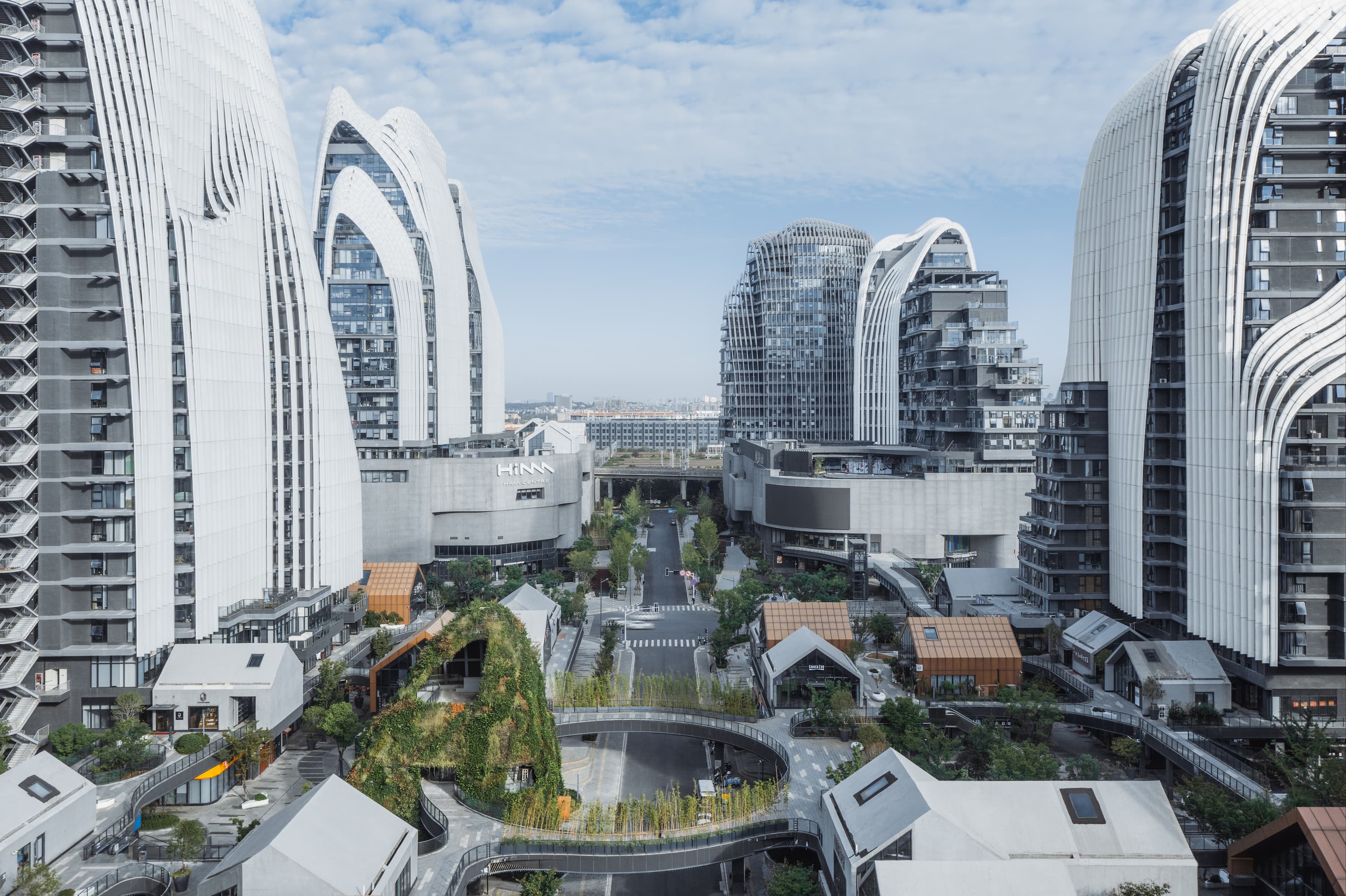 Color photo of the Nanjing Zendai Himalayas Center. Towering buildings with articulated white ridges soar above smaller scale buildings and connecting pathways and green spaces in a city center.