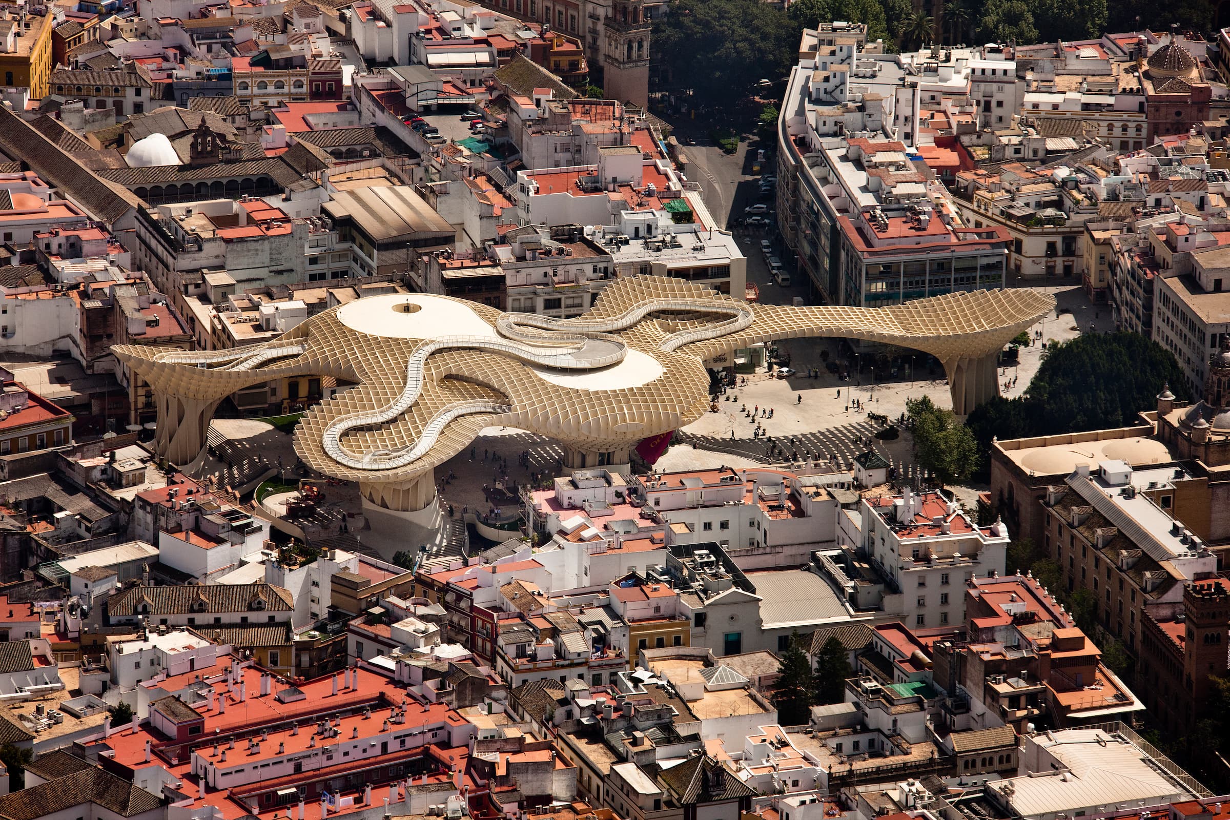 Aerial color photograph of the Metropol Parasol in Seville, Spain. The giant latticed timber canopy is surrounded by the red tiled roofed buildings of the city.