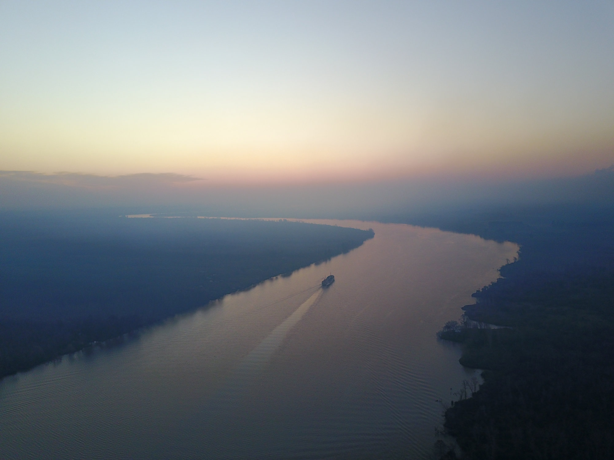 A boat travels through a winding river in a hazy blue and purple landscape under clear skies.
