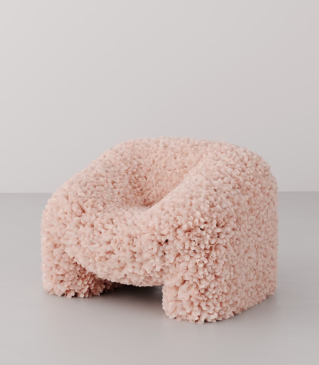 A wide armchair with short, squat legs, and a deeply indented seat. It is upholstered with light, soft-pink polyester petals.