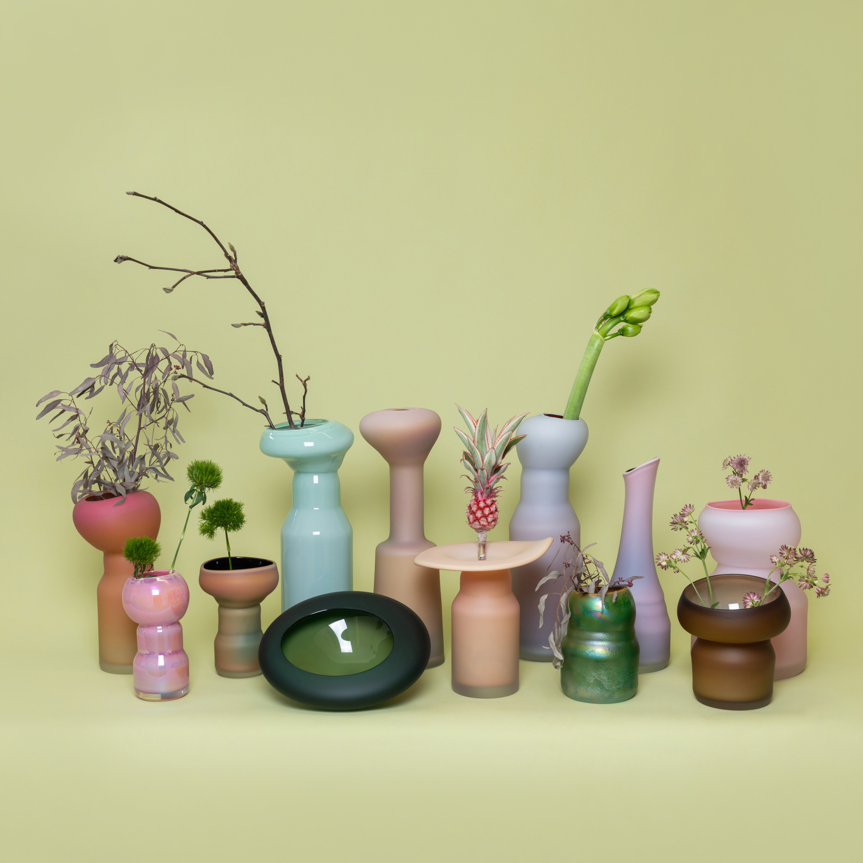 Eleven vases and one bowl inspired by the different shapes of mushrooms in different colors, including orange, pink, turquoise, lavender, dark green, and brown.