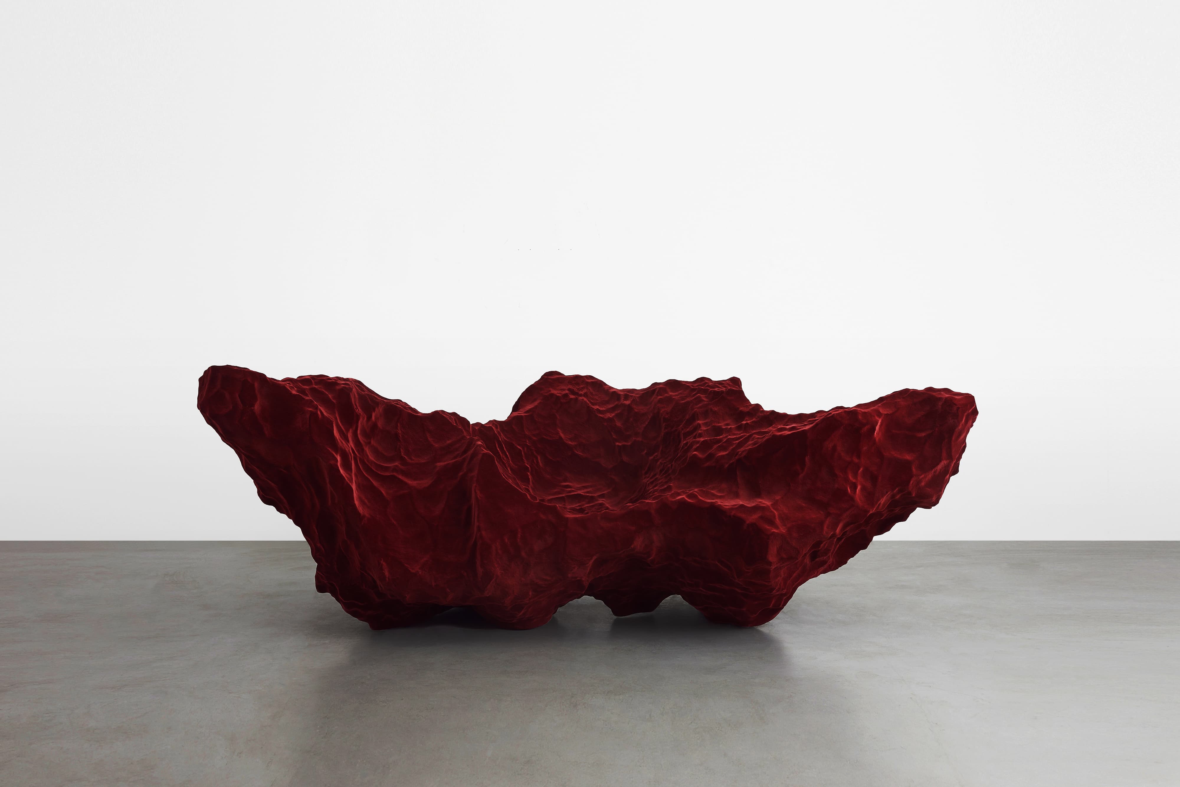 A deep-red sofa that looks as if it is a mountainous rock formation. The jagged, rocky texture of the sofa casts dark shadows and provides a striking contrast in the shades of red.