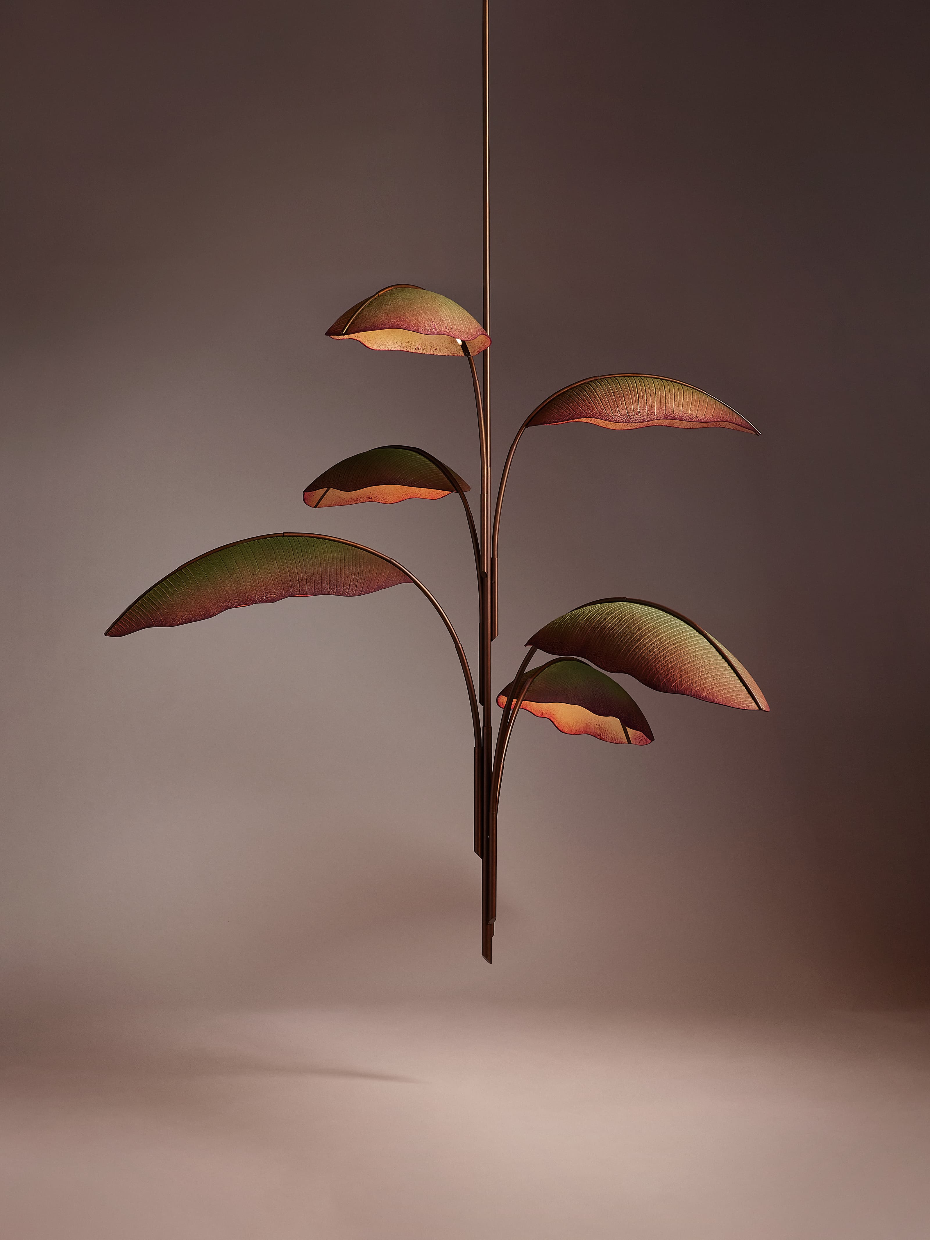 A chandelier with six large leaves radiating out from the center. The centers of the leaves are green, gradually turning a brownish red around the edges. The warm glow of light emanates from under each leaf.