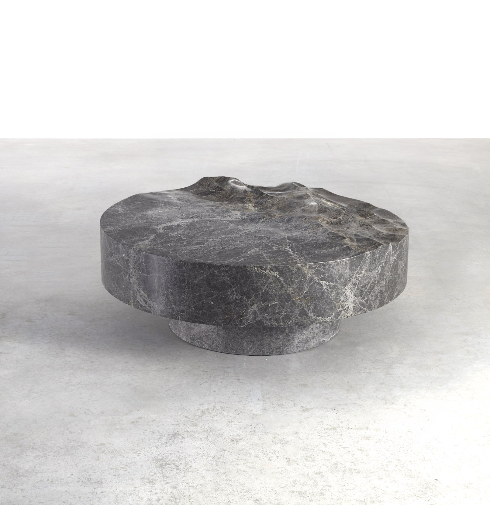 A low, circular table that is gray marble with white striations. This half of the surface looks like gently rolling waves.