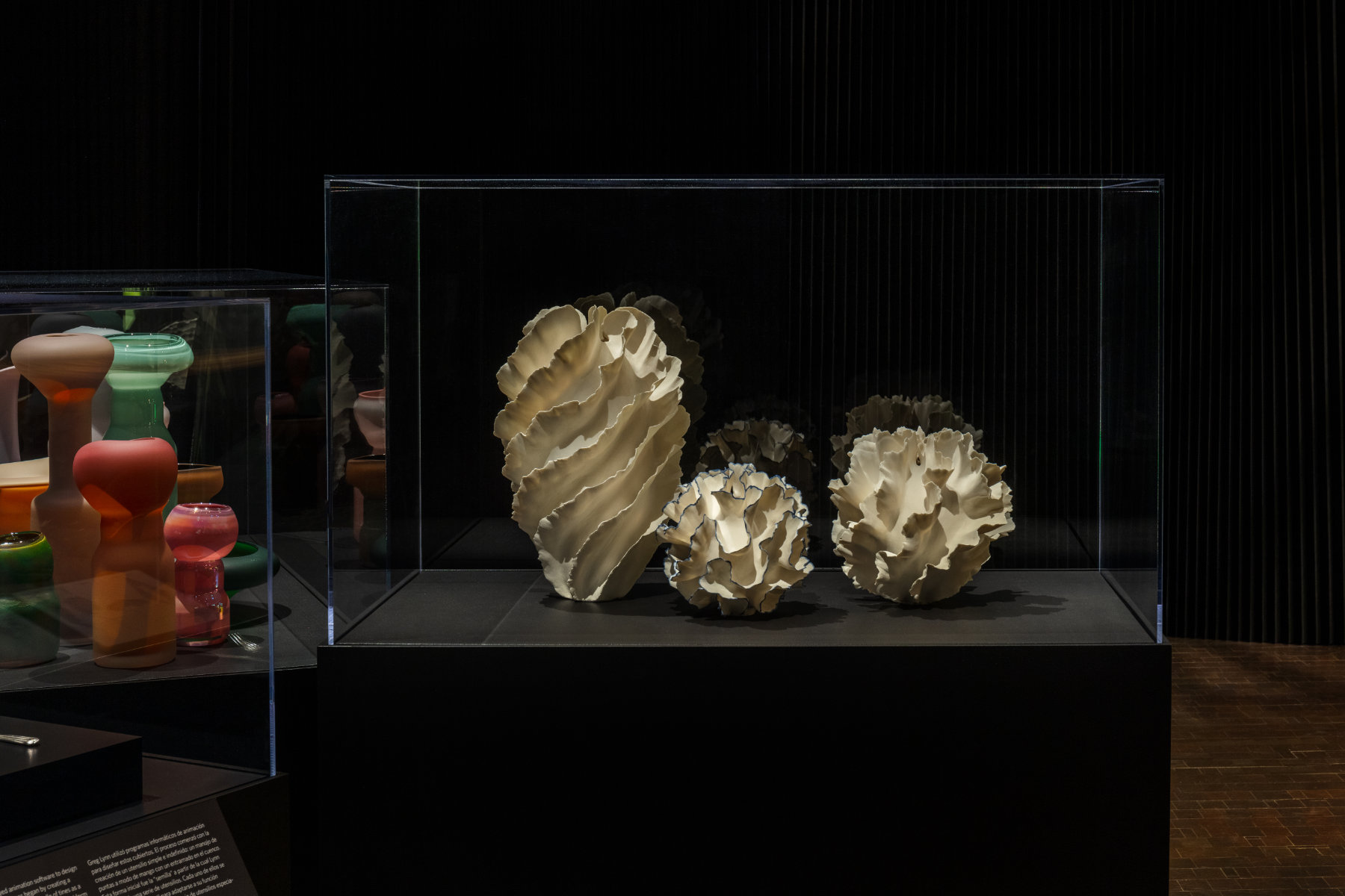 Three pale vessels that evoke the color and patterns of coral are on display in a case against a dark wall.